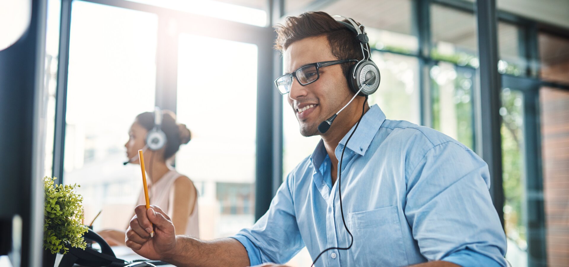 © iStock-1132874986_PeopleImages (Cropped shot of a handsome young man working in a call center with a female colleague in the background)